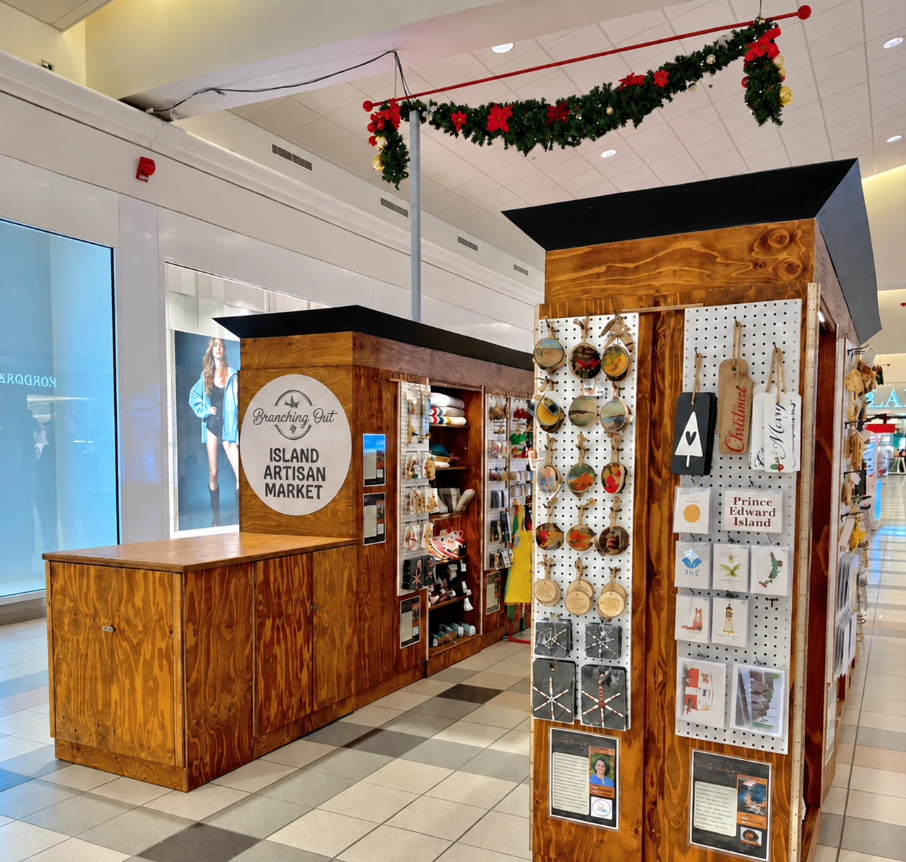 The wooden Branching Out kiosk inside Royalty Crossing Mall, shelves of makers&rsquo; goods and Christmas garland