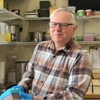 Dennis Hubert in his soap workshop, with shelves of soap behind him