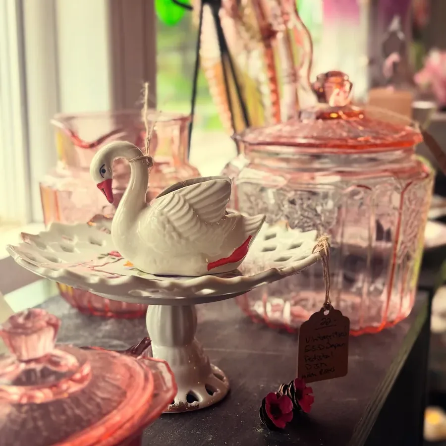 Pink vintage glassware and a white swan dish on a shelf at Sassy Lassie Vintage